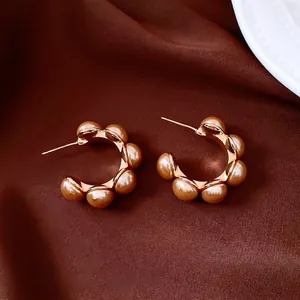 Détail de boucles d'oreilles C dorées à l'or 18K avec perles sur tissu foncé