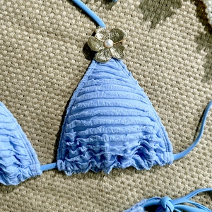 Detail of light blue bikini top with textured frill fabric and gold floral pearl charm