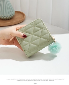 Close-up of a light green quilted short wallet featuring a soft pompom keychain accessory