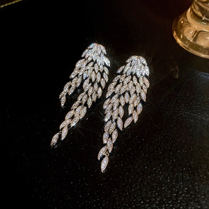 Macro shot of silver feather earrings featuring sparkling crystals on a textured black base