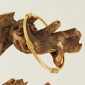 Detailed close-up of 18K gold plated C-shaped bangle on a vintage wooden branch