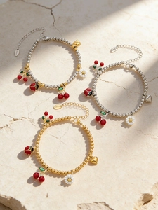 Détail de bracelets en acier avec breloques émaillées en forme de cerise, marguerite et coccinelle
