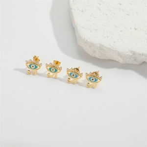 Golden Horus Evil Eye stud earrings with blue enamel and white zircon on white stone background