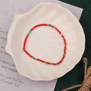 Detail of handmade red and green seed bead bracelet displayed on a shell-shaped ceramic plate