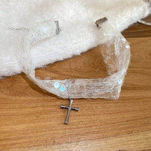 Détail d'un choker en dentelle blanche avec paillettes et pendentif croix en argent