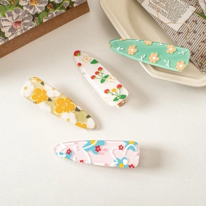 Detailed view of four acrylic hair clips with floral and strawberry patterns