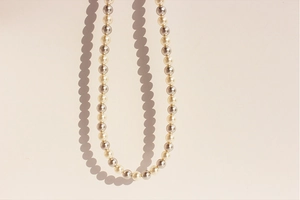 Detail of alternating white and silver-grey round pearls with soft luster on beige surface