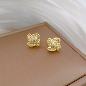 Gold clover stud earrings with white rhinestones on a luxury jewelry display box