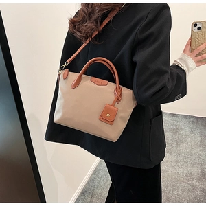 Detail of beige nylon tote bag with brown leather straps and CLEAR'OK brand patch