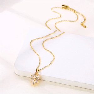 Elegant gold leaf pendant necklace with clear zircon crystals on white pedestal display
