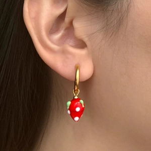 Detail of red heart-shaped enamel earring with white dots on gold plated hoop
