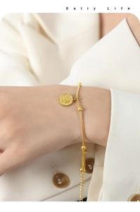 Macro detail of gold coin portrait charm on snake chain bracelet with golden beads