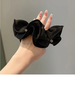 Close-up of black satin scrunchie with rhinestones worn on a wrist for ponytail styling