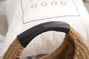 Macro detail of the woven straw bag body with premium black leather handle covers