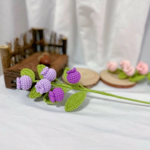 Macro detail of hand-knitted purple crochet flowers with green leaves on white fabric