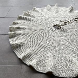 Detailed texture of white knitted Christmas tree skirt with ruffled edge and ties