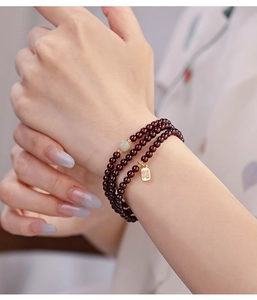 Detail of garnet beaded bracelet with jade bead and gold blessing charm on wrist