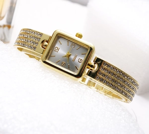 Detail view of square gold quartz watch featuring a crystal-encrusted metal bracelet strap