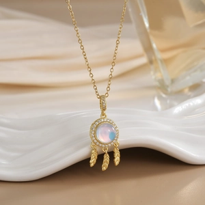 Golden dreamcatcher necklace with moonstone and feathers on white textured pedestal