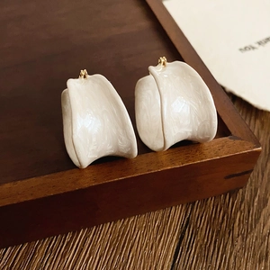 Retro cream white C-shaped resin earrings on a dark wood tray with a golden pin detail