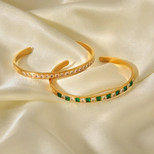 Gros plan de bracelets ouverts en acier doré 18K avec zircons émeraude et blancs élégants