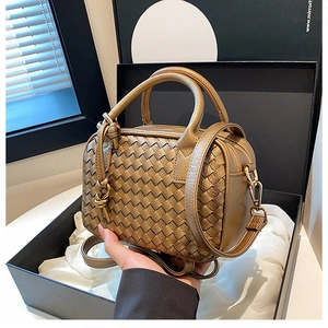 Detail view of gold woven texture Boston bag in elegant gift box with natural light shadows