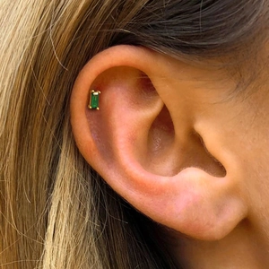 Close-up of a small rectangular green gemstone stud earring in a gold finish setting