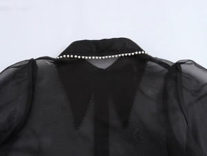 Detailed close-up of white pearl embellishments on a black organza shirt collar
