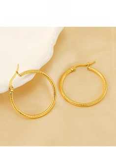 Detailed close-up of gold titanium steel hoop earrings with grooved texture and latch back