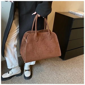 Dettaglio di una borsa tote in pelle scamosciata marrone con un cappotto nero classico