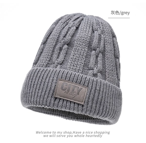 Dettaglio del berretto in maglia grigia a trecce con patch in pelle marrone goffrata