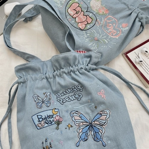 Macro detail of butterfly embroidery and drawstring closure on blue denim tote bag