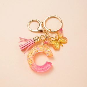Close-up of pink and orange resin letter C keychain with gold leaf, tassel and butterfly