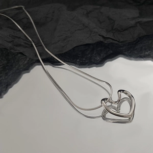Macro shot of silver-colored hollow heart pendant on a thin snake chain over reflective surface