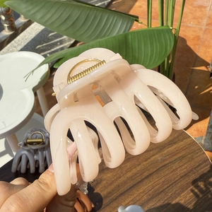 Detailed close-up of a large pale pink resin hair claw clip with golden spring mechanism