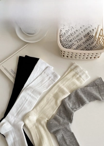 Detailed flat lay of ribbed knee-high socks in black, white, cream, and grey soft cotton