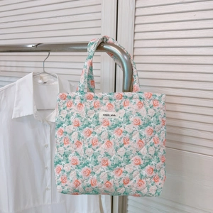 Detailed close-up of floral quilted tote bag with pink rose pattern and logo tag