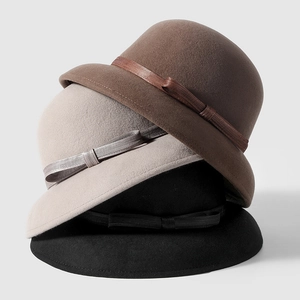 Close-up of three stacked wool cloche hats with decorative ribbon bows in neutral colors
