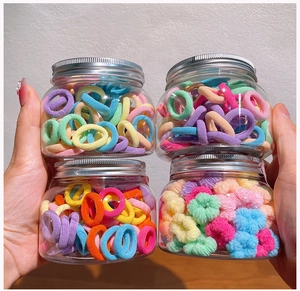 Detailed view of four clear jars filled with colorful elastic hair ties held by hand