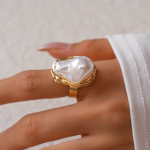 Close-up of a large baroque pearl ring with a textured gold wavy frame on a hand