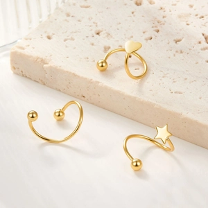 Three gold spiral ear cuffs with heart and star charms on natural stone display