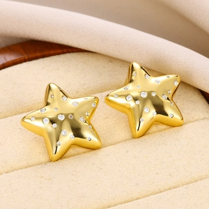 Macro view of gold star stud earrings with sparkling zircon crystals on beige velvet cushion