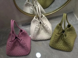 Three woven leather dumpling bags in pink, white and green on marble surface