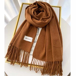 Close-up of caramel cashmere scarf texture with hand-knotted tassels and brand label