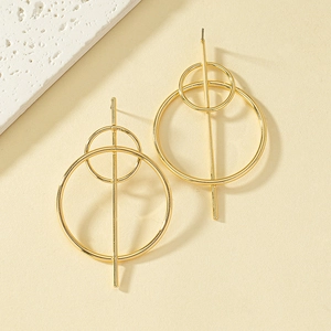 Close-up of golden geometric earrings featuring nested rings on a beige background