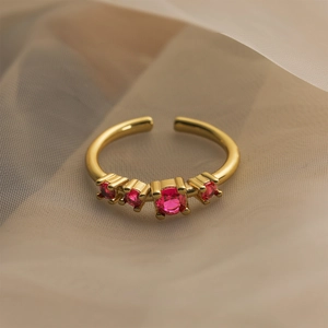 Macro shot of gold-plated ring featuring five ruby-red zircons on beige fabric