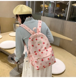 Pink strawberry and heart print backpack shown on person in a cozy interior setting