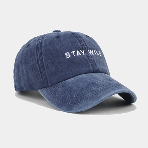 Detailed close-up of white STAY WILD embroidery on washed navy blue denim baseball cap