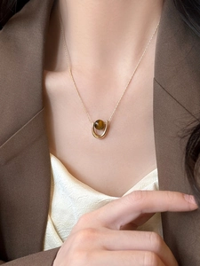 Close-up of golden U-shaped pendant with brown tiger eye stone bead on female model