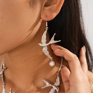 Detailansicht eines vogel-förmigen Ohrrings mit metallischer Textur und Perle